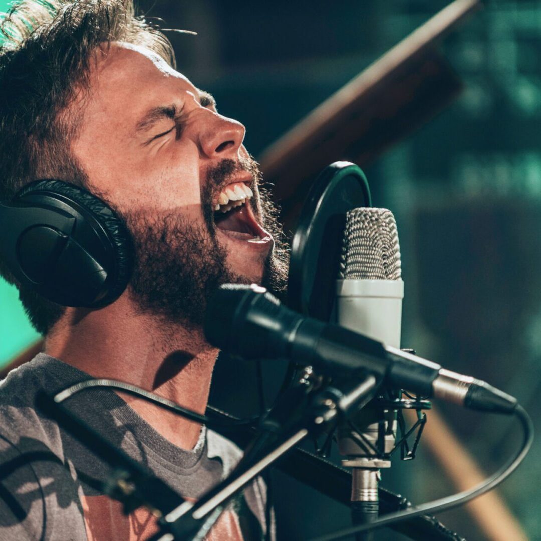 A man with headphones on singing into a microphone.